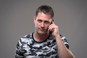 Fototapeta premium Portrait of handsome young adult man talking on the mobile phone and smiling looking at camera over gray background. 