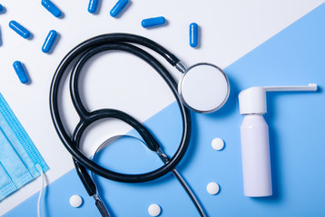 Medecine composition, stethoscope, throat spray, mask, piils, capsule on color white blue background, flat lay, top view