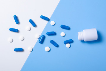 White jar with pills capsule on color white blue background, flat lay, top view