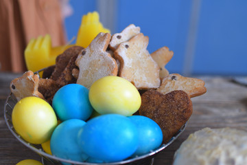 Multi-colored Easter eggs with gingerbread rabbit in metall basket . Yellow, orange and blue.