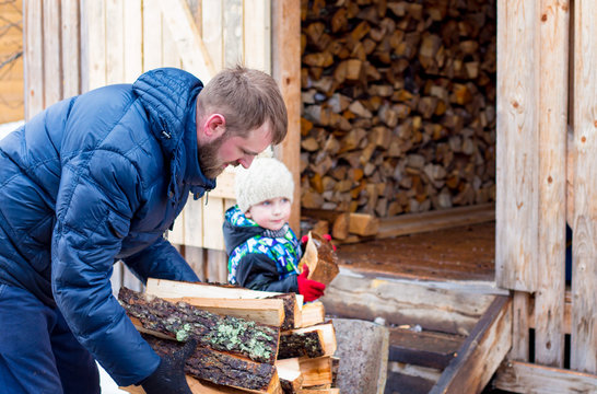 father and little son put just chopped firewood in barn for storing firewood, son helps his father
