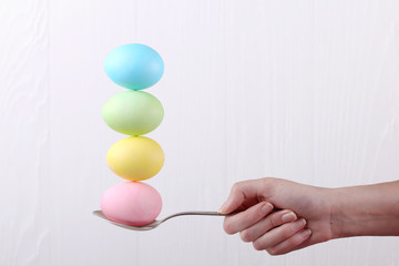 Female hand holds a spoon on which multi-colored eggs are balanced, on a white background. Unusual design, Easter concept, copy space.