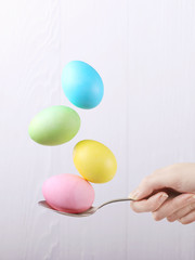Female hand holds a spoon on which multi-colored eggs are balanced, on a white background. Unusual design, Easter concept, copy space.
