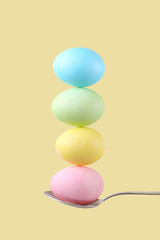 Female hand holds a spoon on which multi-colored eggs are balanced, on a yellow background. Unusual design, Easter concept, copy space.