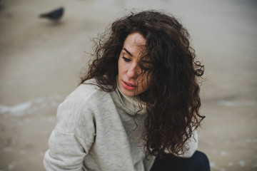 Portrait of young curly woman in beige sweater on sea beach background