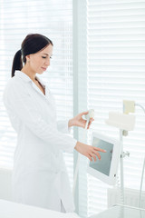 Obraz na płótnie Canvas Young beautiful aesthetic medicine female doctor in white outfit standing near hardware cosmetology apparatus in dermatology clinic.