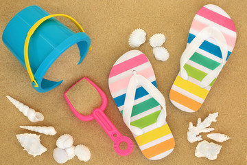 Summer vacation at the beach concept with rainbow coloured flip flops, seashells and bucket and spade on sand beach.