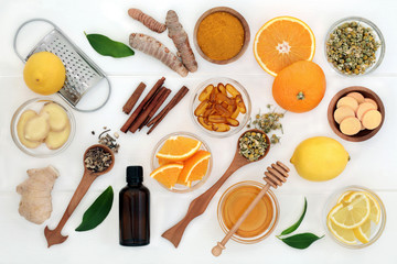 Ingredients for cold and flu remedy with ginger, turmeric, echinacea, chamomile and cinnamon, eucalyptus oil, honey, vitamin tablets and capsules with orange and lemon fruit on white wood.