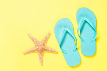 Blue flip flops and starfish on yellow background. 