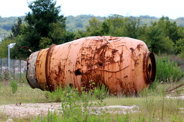 Obraz premium Destroyed rusted with multiple holes cement mixer truck drum taken off truck and discarded in nature surrounded with high uncut grass and forest in background on warm sunny day