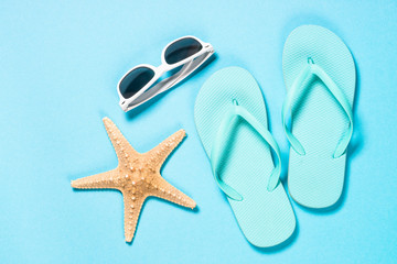 Blue flip flops, sunglasses and starfish on blue background.
