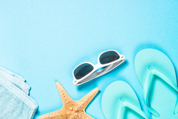 Blue flip flops, sunglasses and starfish on blue background.