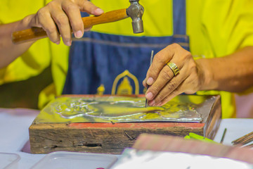 Close up Thai engraver while craving silver pattern with hammer and chisel at night. Silversmith craftsman carving pattern on a silver plate.