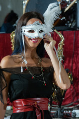 Smiling sexy woman with white carnival mask with feather. Black dress with red band with open shoulders. Venetian carnival Background with musical instruments. Fashion, Valentine's Day, Brazil, Italy 