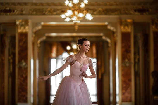 Beautiful ballerina dancing in a luxurious hall in a pink dress.