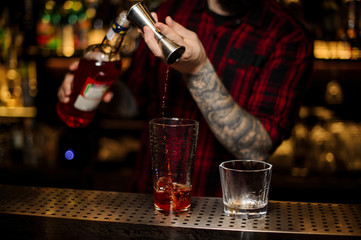 Bartender pouring a drink making Foreign Legion cocktail from the steel jigger to the measuring cup