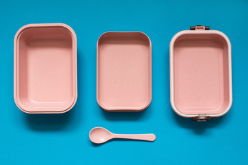 Empty pink bento lunch box with spoon on blue background