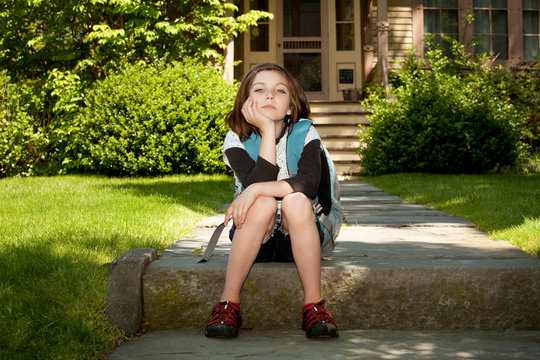 Girl (8-9) waiting for school bus in front of house 