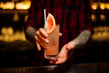 Bartender serving a glass of a delicious cocktail with grapefruit on the bar counter