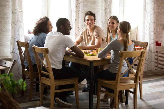 Multiracial laughing friends having fun together, talking in cafe