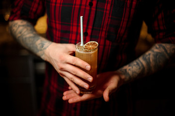 Bartender serving a glass of a Singapore Sling cocktail with orange zest