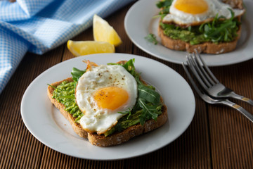 Sandwich or bread toast with avocado and a fried egg on a white plate on rustic wood table. Healthy food. Healthy eating.