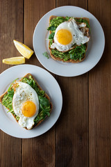 Sandwich or bread toast with avocado and a fried egg on a white plate on rustic wood table. Healthy food. Healthy eating.