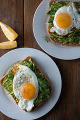 Sandwich or bread toast with avocado and a fried egg on a white plate on rustic wood table. Healthy food. Healthy eating.