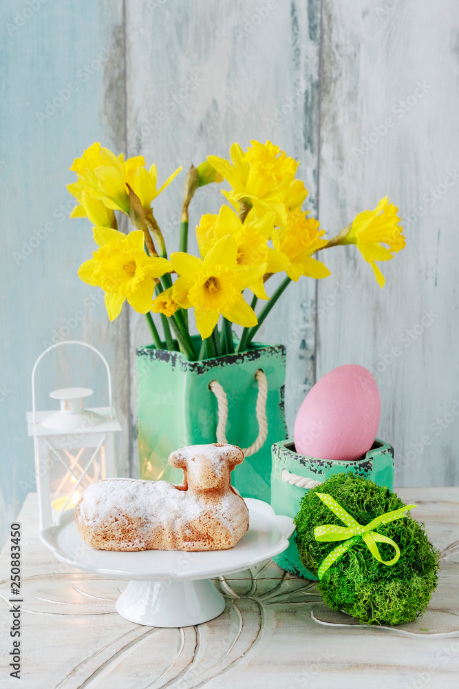 Sticker easter table with lamb cake, bouquet of daffodils and painted eggs.