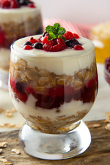 Glass jar withovernight oats, granola and yogurt with berry, raspberries and blackberries on wooden cutting board over wooden background. Healthy food.