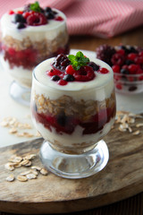 Glass jar withovernight oats, granola and yogurt with berry, raspberries and blackberries on wooden cutting board over wooden background. Healthy food.