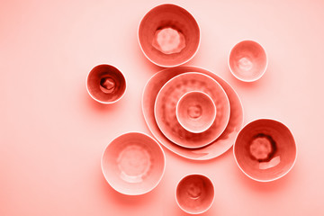 Beautiful dinnerware, plates bowls on pink table, top view, selective focus. Photo toned in trendy coral tones, color of the year 2019