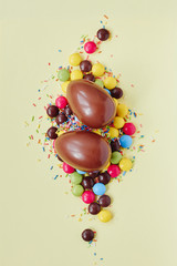 Chocolate Easter eggs and sweets on pastel yellow background