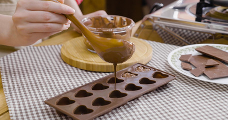 woman hand put curd filling in silicone mold smeared with melted dark chocolate liquid. female...