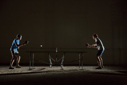 Two men playing table tennis at night 