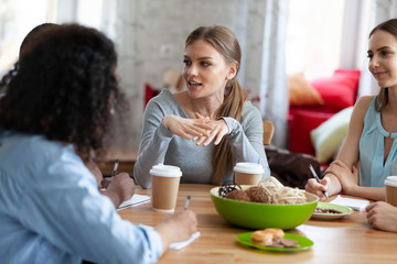 Attractive girl sharing ideas, doing homework with friends in cafe