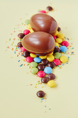 Chocolate Easter eggs and sweets on pastel yellow background