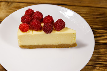 Piece of tasty New York cheesecake with raspberries in a white plate on wooden table