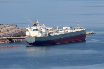 International oil tanker parked in local harbour waiting to be unloaded surrounded with calm dark blue sea and stone shore on warm sunny day