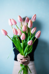 Young woman holding a beautiful bunch of tulips in her hands. Spring present for a girl in a grey dress. Flowers bouquet.