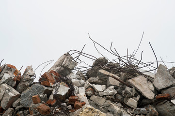 The rebar sticking up from piles of brick rubble, stone and concrete rubble against the sky in a...