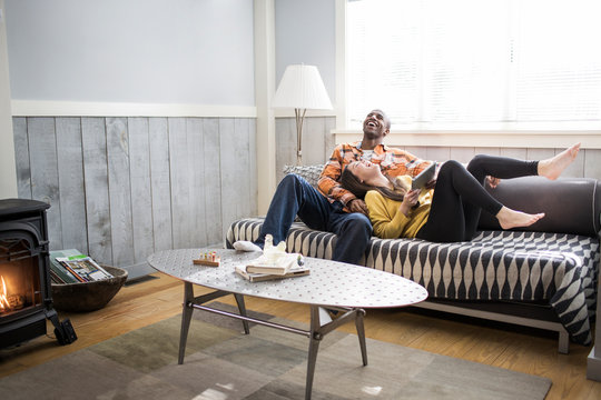 Smiling Young Couple With Digital Tablet Relaxing On Sofa At Home