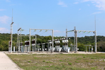 Fototapeta na wymiar Local power plant dense array of support electrical equipment on strong metal supports made of various devices with dark brown ceramic and glass insulators connected with electrical wires surrounded w