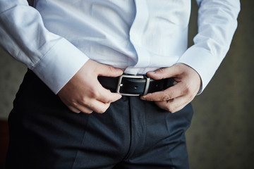 Businessman putting on a belt, fashion and clothing concept,groom getting ready in the morning before ceremony