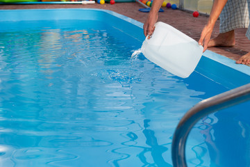 men's hands pour light liquid from a plastic tank into a pool, into water. chemical water purification, alkali balance, unsanitary conditions. disinfection and preparation for swimming. 