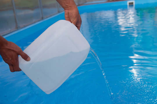 men's hands pour light liquid from a plastic tank into a pool, into water. chemical water purification, alkali balance, unsanitary conditions. disinfection and preparation for swimming. 