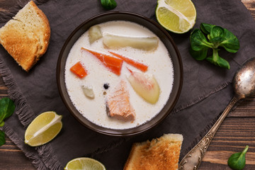 Creamy salmon soup with potatoes and carrots served with toast on a wooden rustic plank table. Finnish fish soup kalakeitto with salmon. Top view.