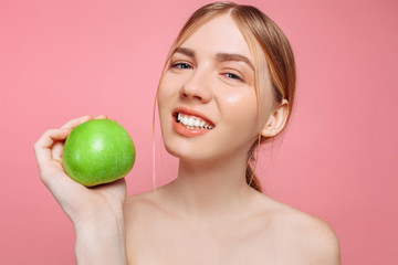 Portrait of a happy beautiful woman holding an apple, on a pink background