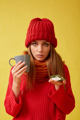 Sick girl holding pills and a cup in her hands. Image on yellow background.