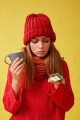 Sick girl holding pills and a cup in her hands. Image on yellow background.
